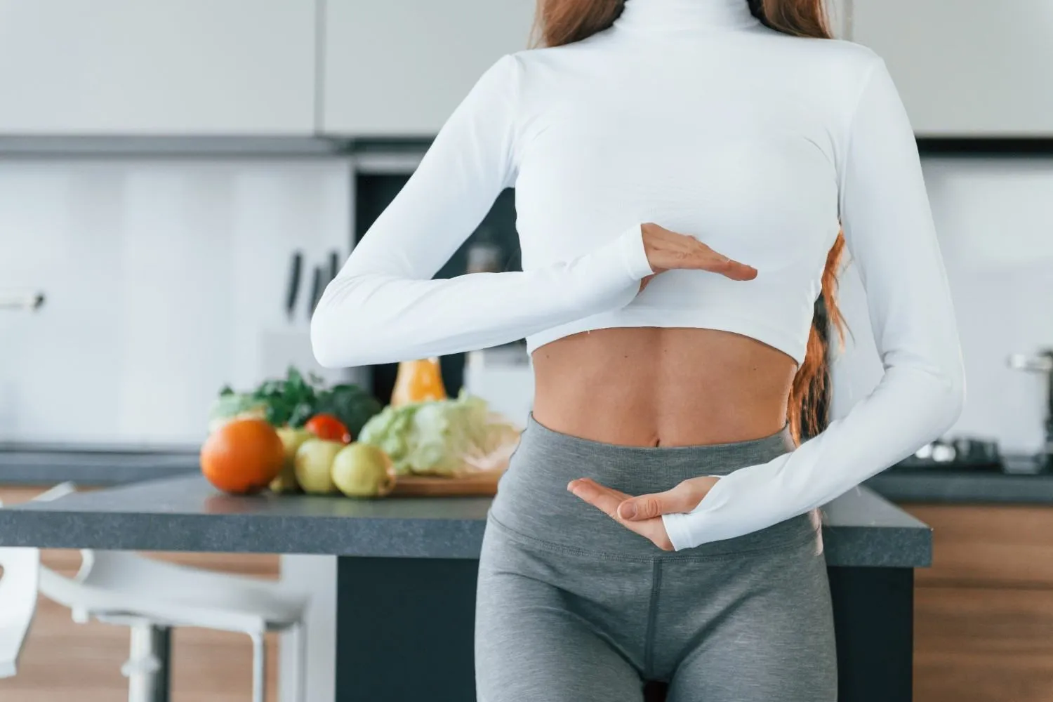 Woman framing her midsection in a kitchen full of fresh vegetables
