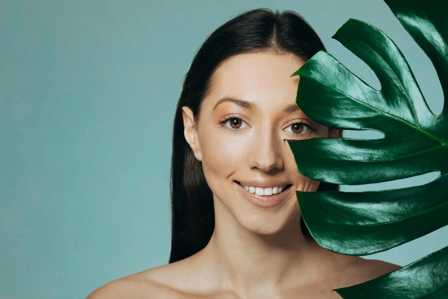 Woman with clear skin holding a green leaf beside her face