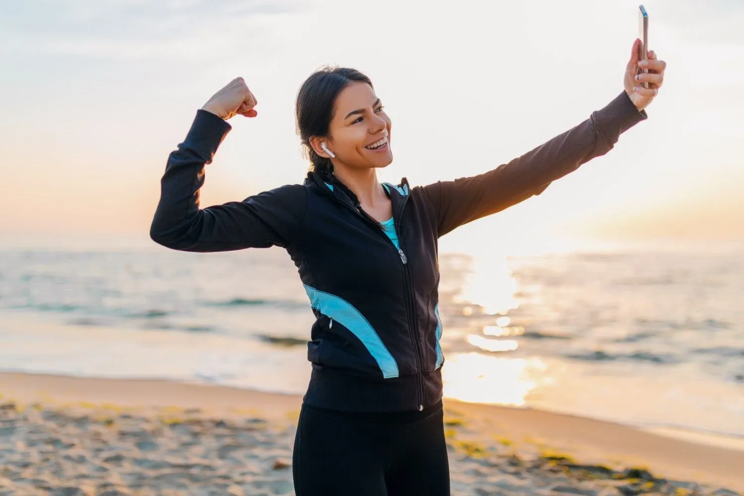 Woman flexing her arms on a beach at sunrise